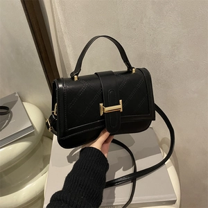 Chic black quilted crossbody bag with gold buckle and top handle in a lifestyle setting