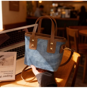 Detail of blue denim mini tote bag with brown leather trim and golden metal rivets