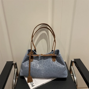 Sac fourre-tout bleu à motif léopard avec bandoulières marron sur une chaise en cuir noir
