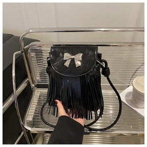 Detail of black crossbody bag with silver metal bow and long stylish fringe accents