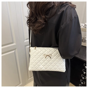 Detail of white quilted crossbody bag featuring a golden bow metal accessory on the front