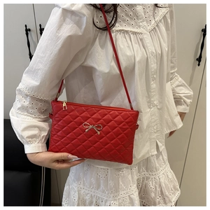 Detail of red quilted shoulder bag with golden metal bow and smooth zipper closure