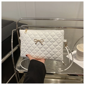 Detail of white quilted crossbody bag with gold metal bow and elegant chain strap