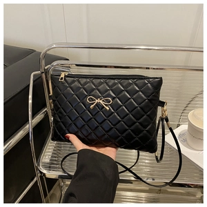 Macro detail of quilted crossbody bag featuring a golden metal bow and black faux leather