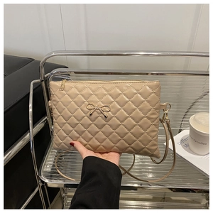 Detail of beige quilted crossbody bag with a gold metal bow accent and chain strap