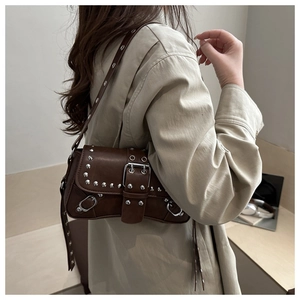 Side view of dark brown punk style shoulder bag with silver rivets on beige coat