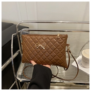 Detail of a brown quilted crossbody bag with golden bow hardware and leather strap