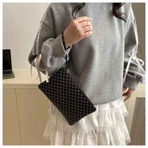 Detail of minimalist black monogram clutch bag with geometric pattern and wristlet strap