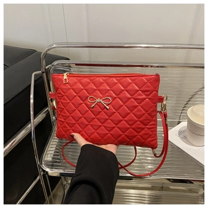 Detail of red quilted crossbody bag featuring a gold metal bow and sleek rhombus stitching