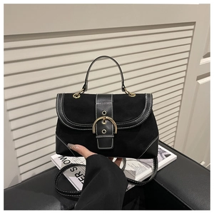 Detailed view of black crossbody bag with large gold buckle and contrast white stitching