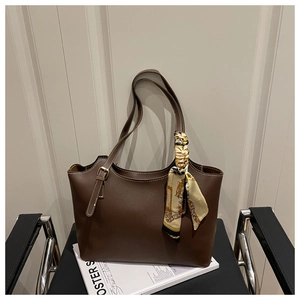 Detail view of coffee brown faux leather tote bag with white stitching and decorative scarf
