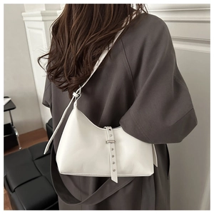 Close-up of cream white leather shoulder bag with decorative rivet strap on a model