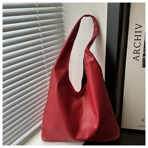 Close-up of a red minimalist tote bag made of smooth leather leaning against a white wall