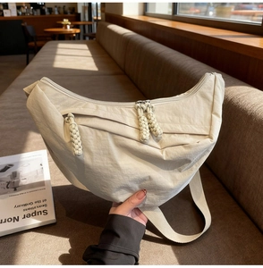 Detail of a creamy nylon crescent bag with woven zipper pull on a cafe bench