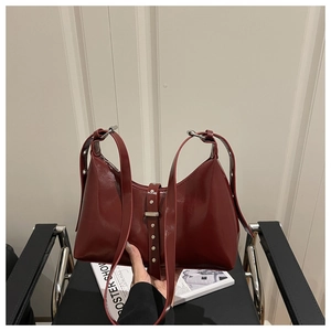 Detail of burgundy glossy leather handbag with silver rivets and adjustable strap