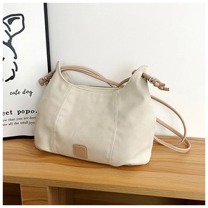 Detail of a creamy white crescent hobo bag with knotted straps on a wooden table