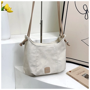 Detail of cream shoulder bag with side drawstring, silver beads, and Fashion logo patch