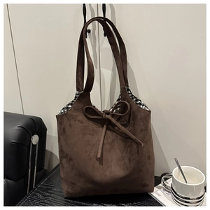 Detail of dark brown suede tote bag featuring a decorative bow and plaid lining fabric