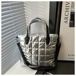 Detail of silver metallic quilted tote bag featuring black handles and detachable shoulder strap