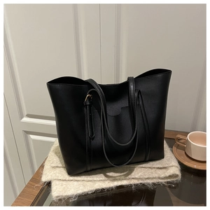 Detailed view of black matte PU leather tote bag with long straps on beige knit scarf