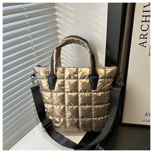 Detailed close-up of metallic gold quilted puffer tote bag with black strap in natural light