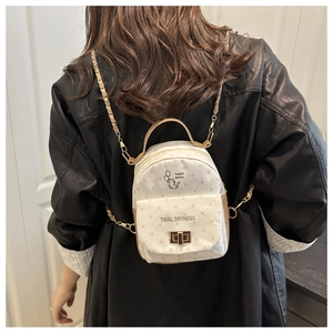 Detail of white polka dot mini backpack with golden chain strap and cat logo