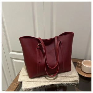 Detail view of burgundy tote bag with handles on white wooden and grey fabric background