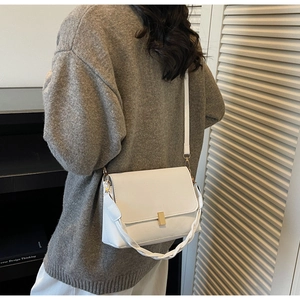Detail of white leather shoulder bag with gold clasp and woven handle on a grey sweater
