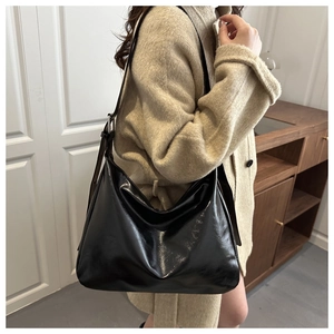 Glänzende schwarze Hobo-Tasche mit verstellbarem Riemen auf einem beigen Wollmantel
