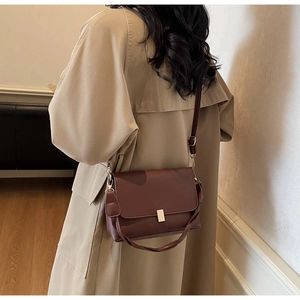 Close-up of a deep brown leather crossbody bag with a golden metal buckle on a beige coat