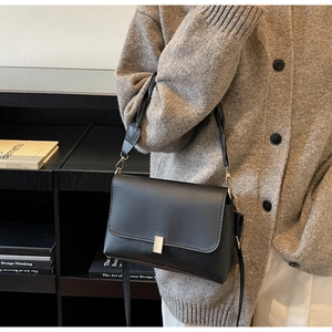 Close-up of a black leather square bag with a golden buckle worn with a brown cardigan