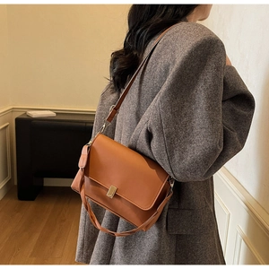Detail of caramel brown leather shoulder bag with golden metallic lock on a grey blazer