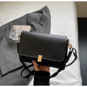 Detail of minimalist black crossbody bag with gold buckle and matte leather texture