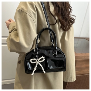 Detail of black patent leather Boston bag with shiny finish and beaded bow charm