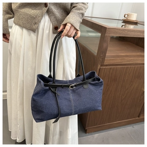 Close-up of blue denim tote bag with leather belt detail and golden buckle accent