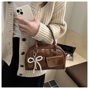 Detail of brown patent leather Boston bag with pearl bow charm and twin front pockets