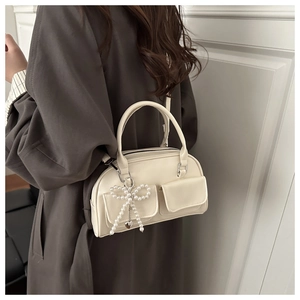 Detail of cream Boston bag featuring pearl bow charm and twin front flap pockets