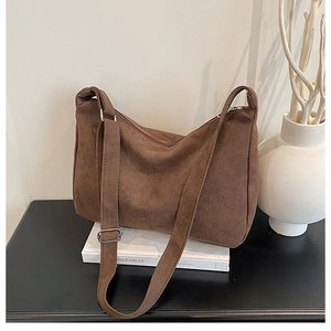 Détail d'un grand sac bandoulière en daim marron avec livre et vase minimaliste