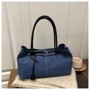 Detail of dark blue denim tote bag featuring white stitching and black leather handle straps