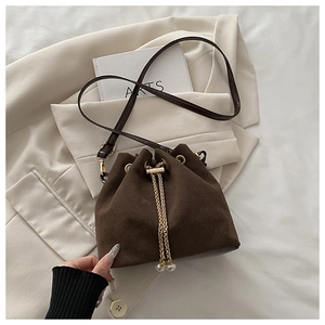 Macro detail of brown suede bucket bag featuring gold drawstrings and pearl charms