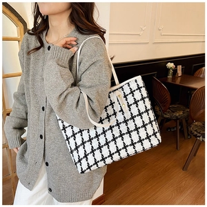 Close-up of stylish black and white woven tote bag with white leather handle and rivets