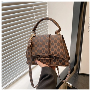 Close-up of brown M-patterned handbag showing gold clasp and luxury synthetic leather texture