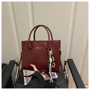 Detail of burgundy faux leather tote bag with gold lettering and woven charm pendant
