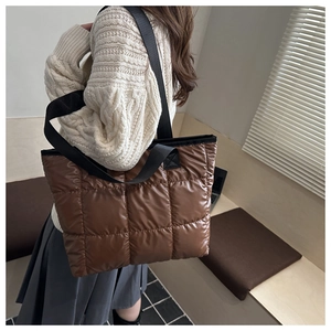 Detail of a brown quilted puffer tote bag with glossy finish and wide square stitching