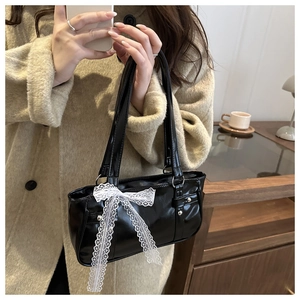 Detail of black glossy leather shoulder bag with white lace bow on the front