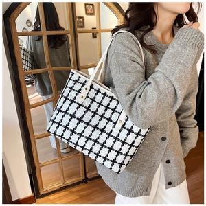 Detail of checkered tote bag with white strap and gold rivets on tweed fabric