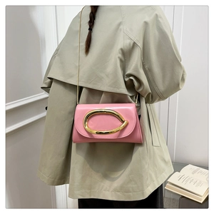 Pink patent leather crossbody bag with oversized gold oval buckle on trench coat outfit