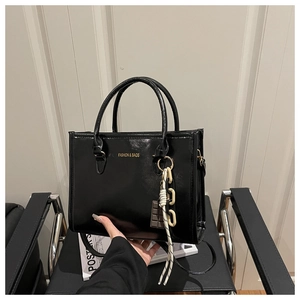 Detail of black glossy PU leather tote bag with gold logo and stylish chain keychain