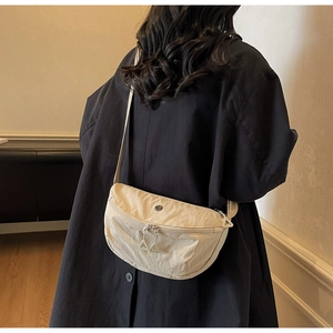 Close-up of a beige crescent nylon crossbody bag with dual zippers on a model
