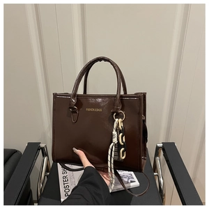 Detail view of deep brown glossy tote bag with gold lettering and woven chain charm